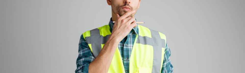 unsure young male engineer wearing safety helmet and uniform holding note pad and pencil keeping hand on chin looking up isolated on white background