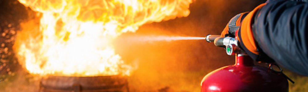 A man aiming water from the hose of a fire extinguisher at a fire.